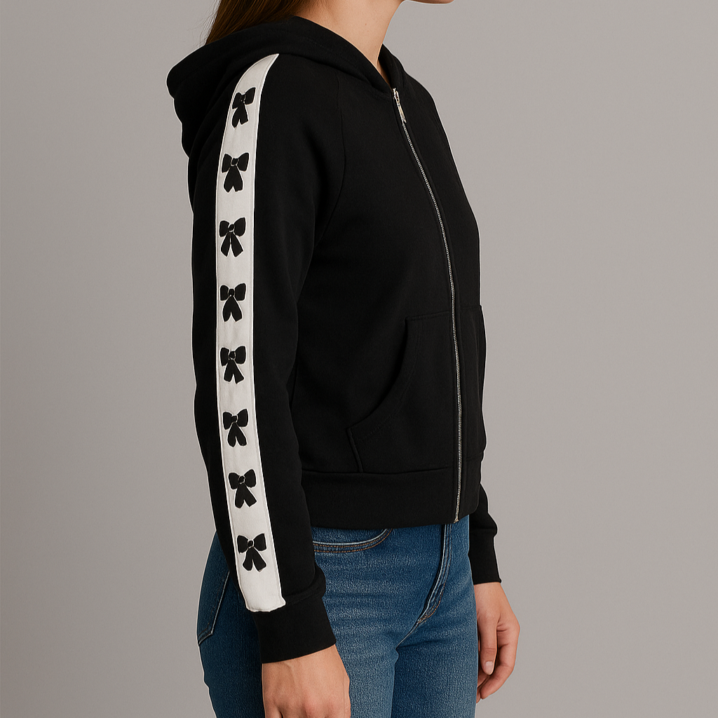 Woman wearing a black hoodie with white bow designs on sleeves against a gray background
