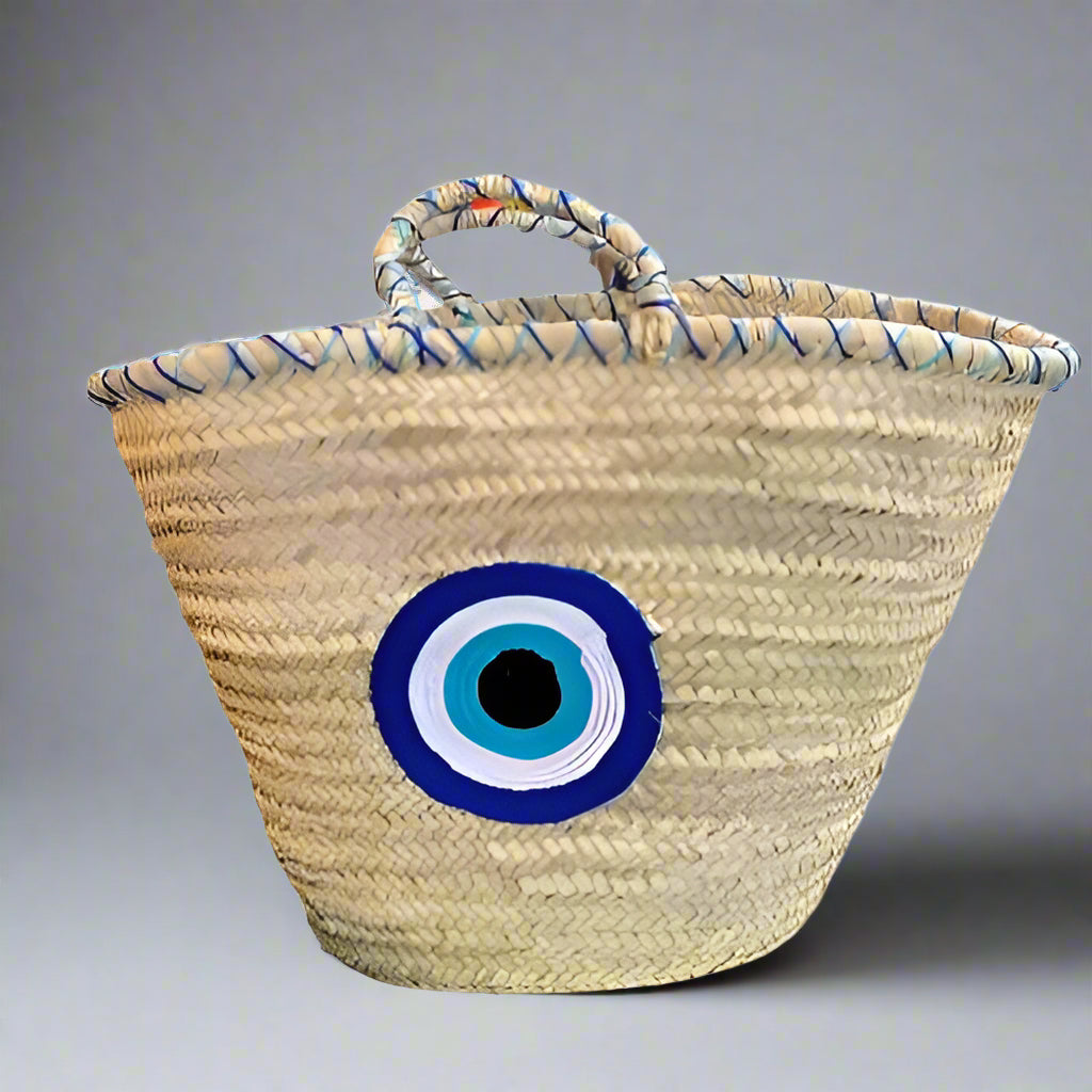 A beige straw bucket bag with a blue and black evil eye design on the front.