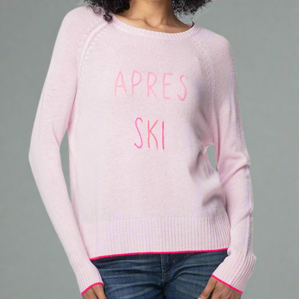 Pink sweater with 'APRES SKI' text worn by a person on a gray background