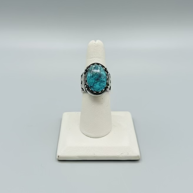 Turquoise ring on a white stand with a laptop and phone in the background