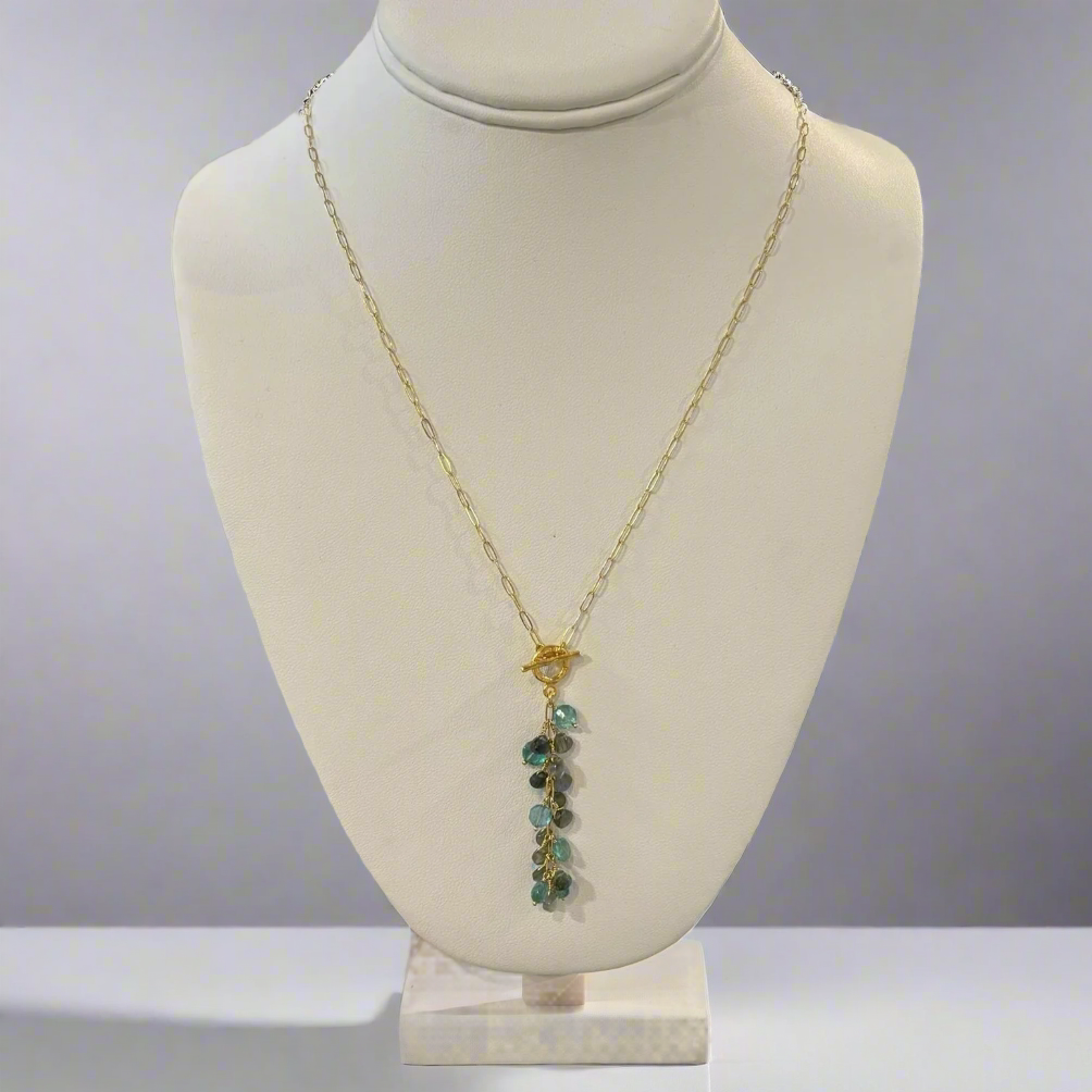 A labradorite necklace displayed on a mannequin bust, featuring a gold-colored chain and a teardrop-shaped pendant with multiple faceted surfaces.