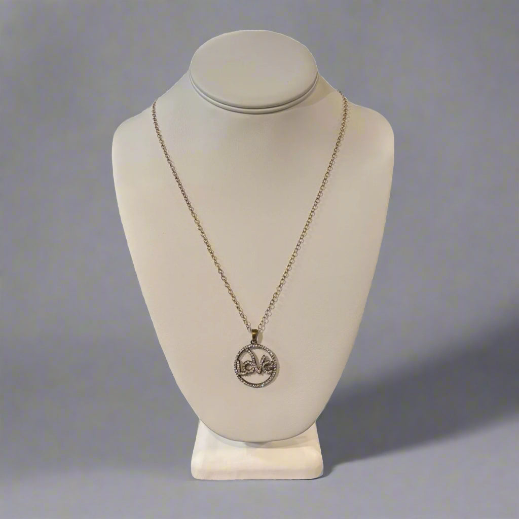 A gold-colored necklace with a round 'LOVE' charm displayed on a mannequin bust.