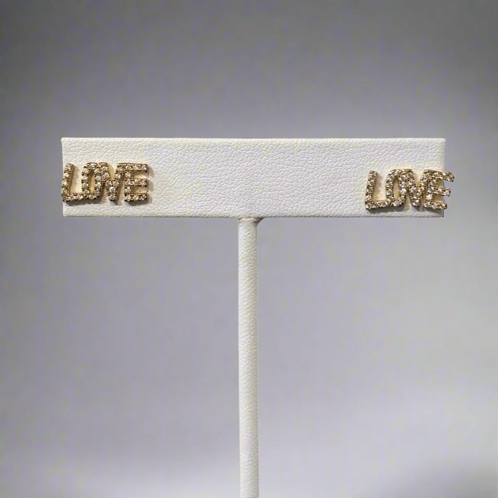 A silver-colored brooch with the word 'LOVE' in capital letters, featuring a textured surface and small gold-tone accents.