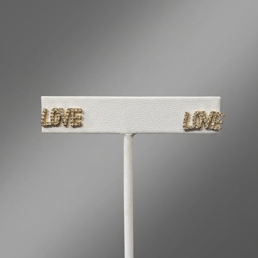 A silver-colored brooch with the word 'LOVE' in capital letters, featuring a textured surface and small gold-tone accents.