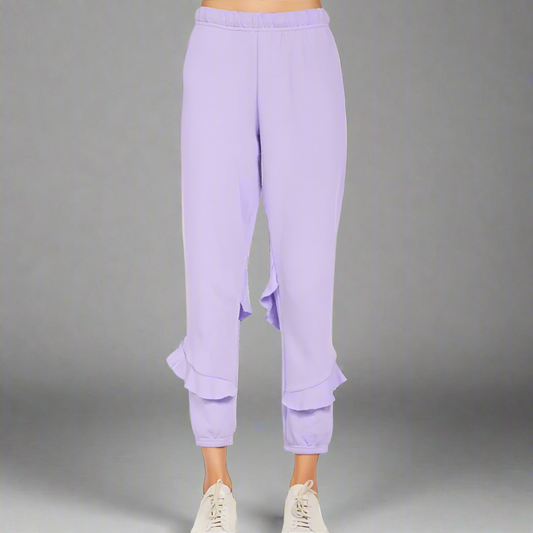 A person standing wearing purple ruffle sweatpants and white sneakers.