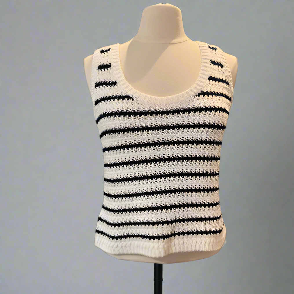 Woman wearing a white crochet tank top with black stripes on a blackq background