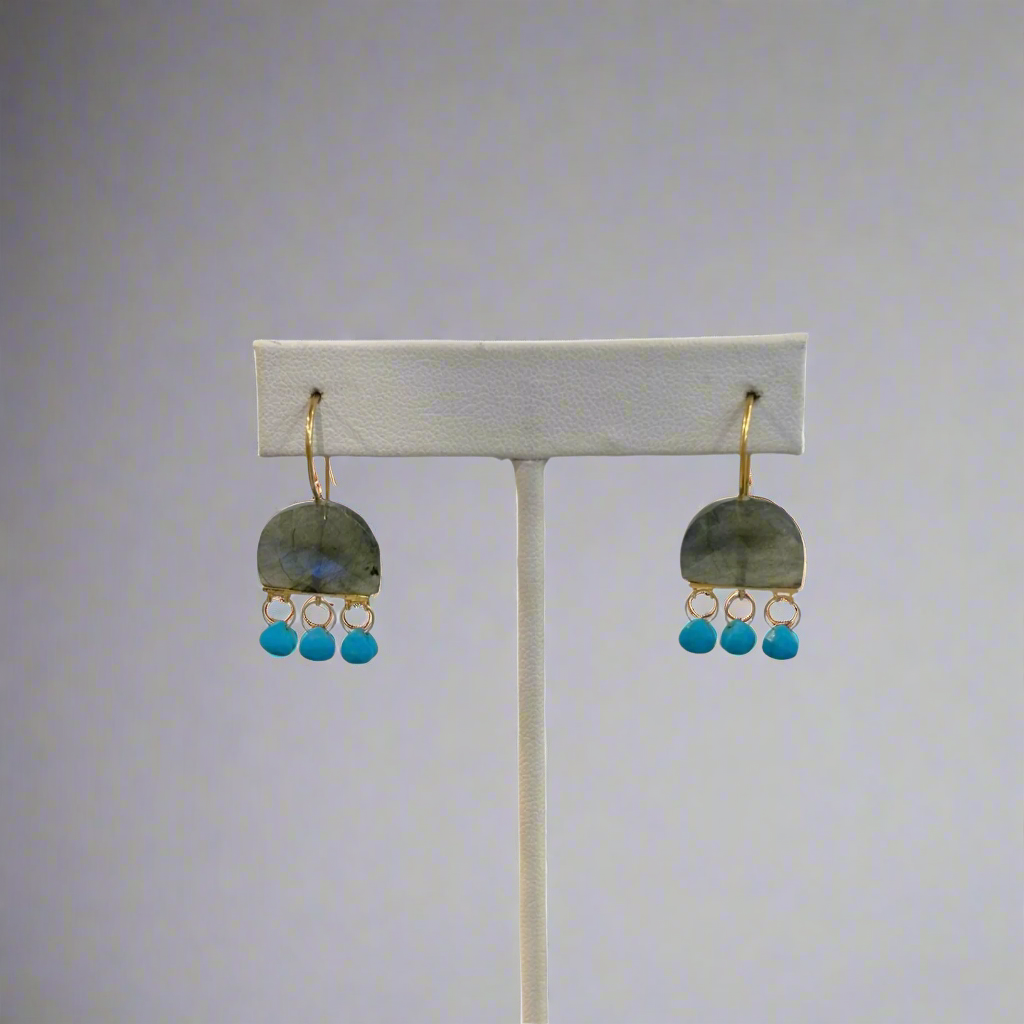 A pair of labradorite earrings displayed on a white stand with gold-colored clasps.