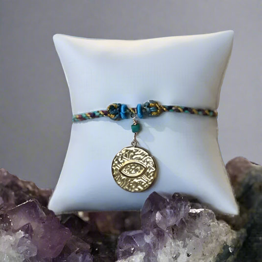 Bracelet with a gold eye pendant on a white pillow, set against an amethyst crystal base.
