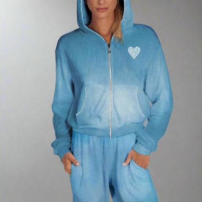 A woman wearing a blue cropped zip-up hoodie with a heart-shaped detail on the back and a diamond pattern around the eye area.