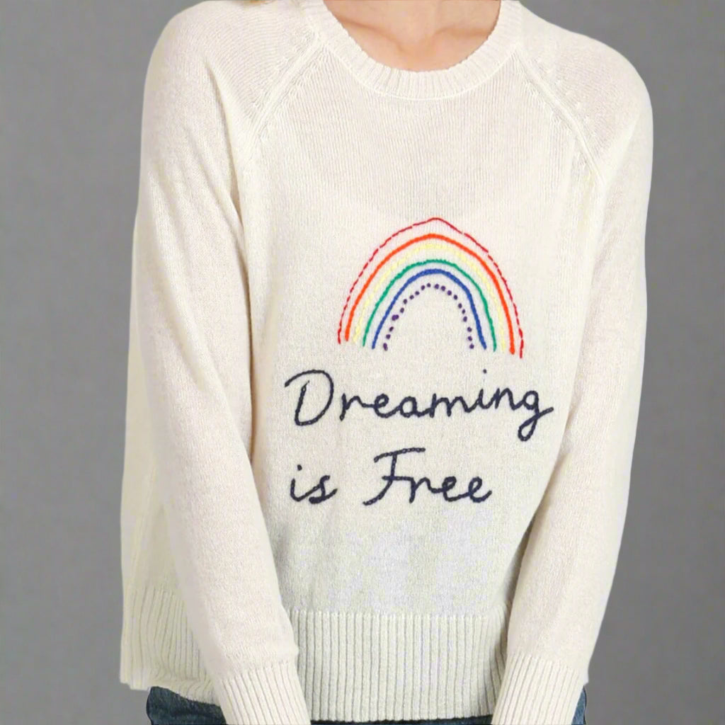White sweater with rainbow and 'Dreaming is Free' text on a white background