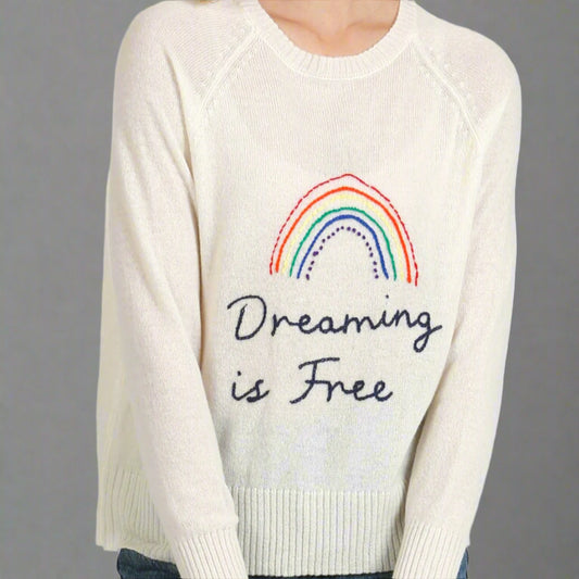 White sweater with rainbow and 'Dreaming is Free' text on a white background