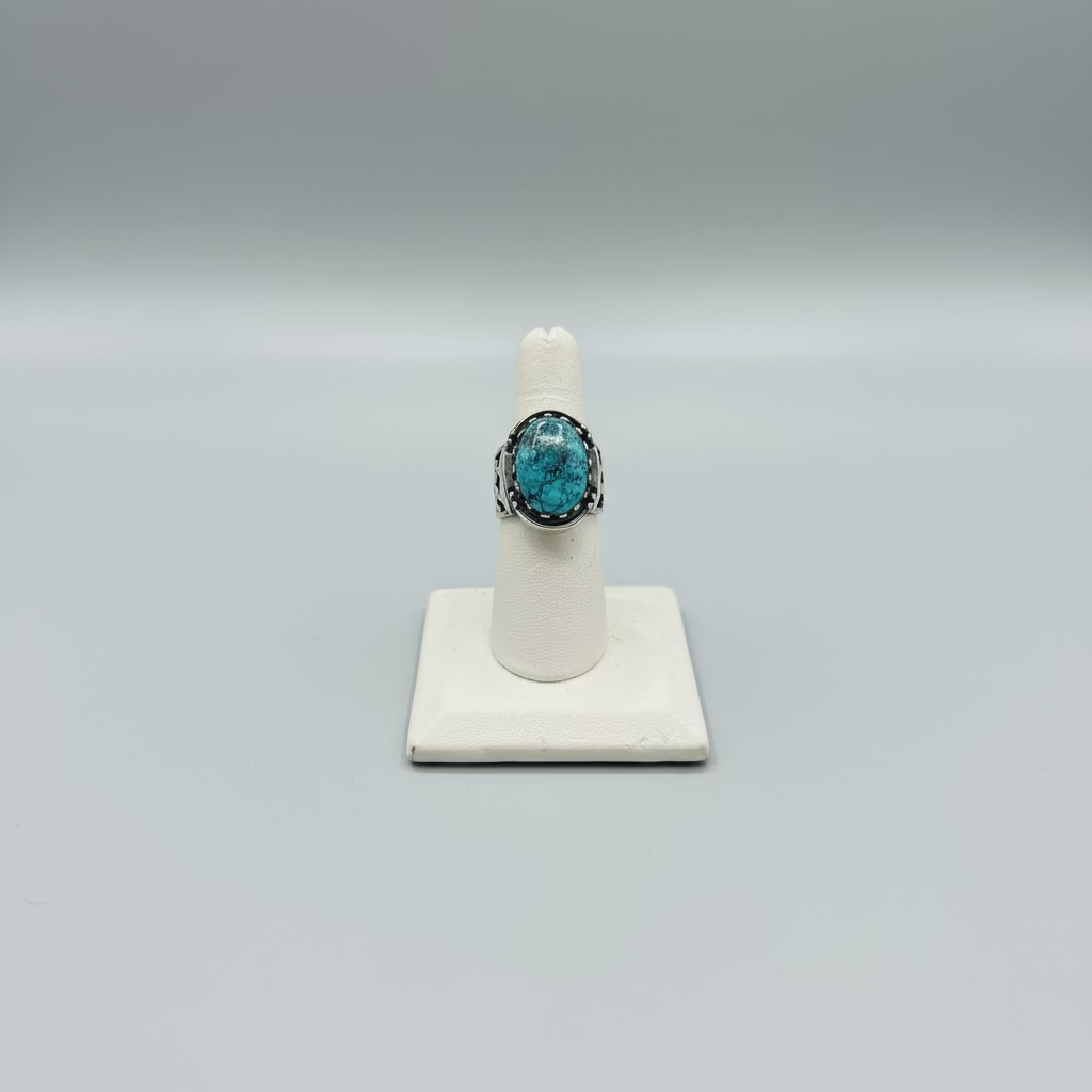 Turquoise ring on a white stand with a laptop and phone in the background