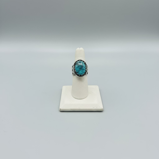 Turquoise ring on a white stand with a laptop and phone in the background