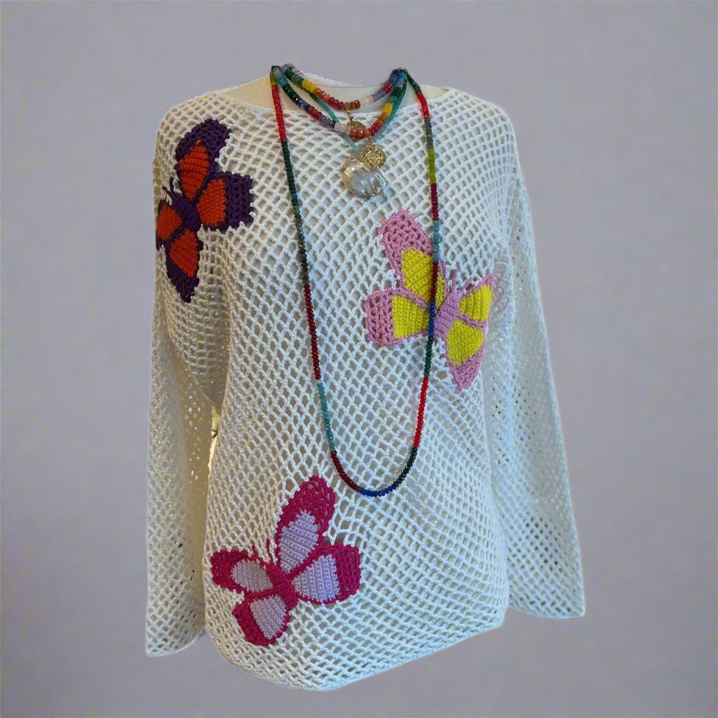 A white crochet pullover with colorful butterfly details and beaded necklaces displayed on a mannequin.