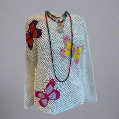A white crochet pullover with colorful butterfly details and beaded necklaces displayed on a mannequin.