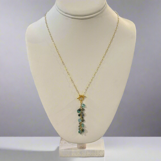 A labradorite necklace displayed on a mannequin bust, featuring a gold-colored chain and a teardrop-shaped pendant with multiple faceted surfaces.