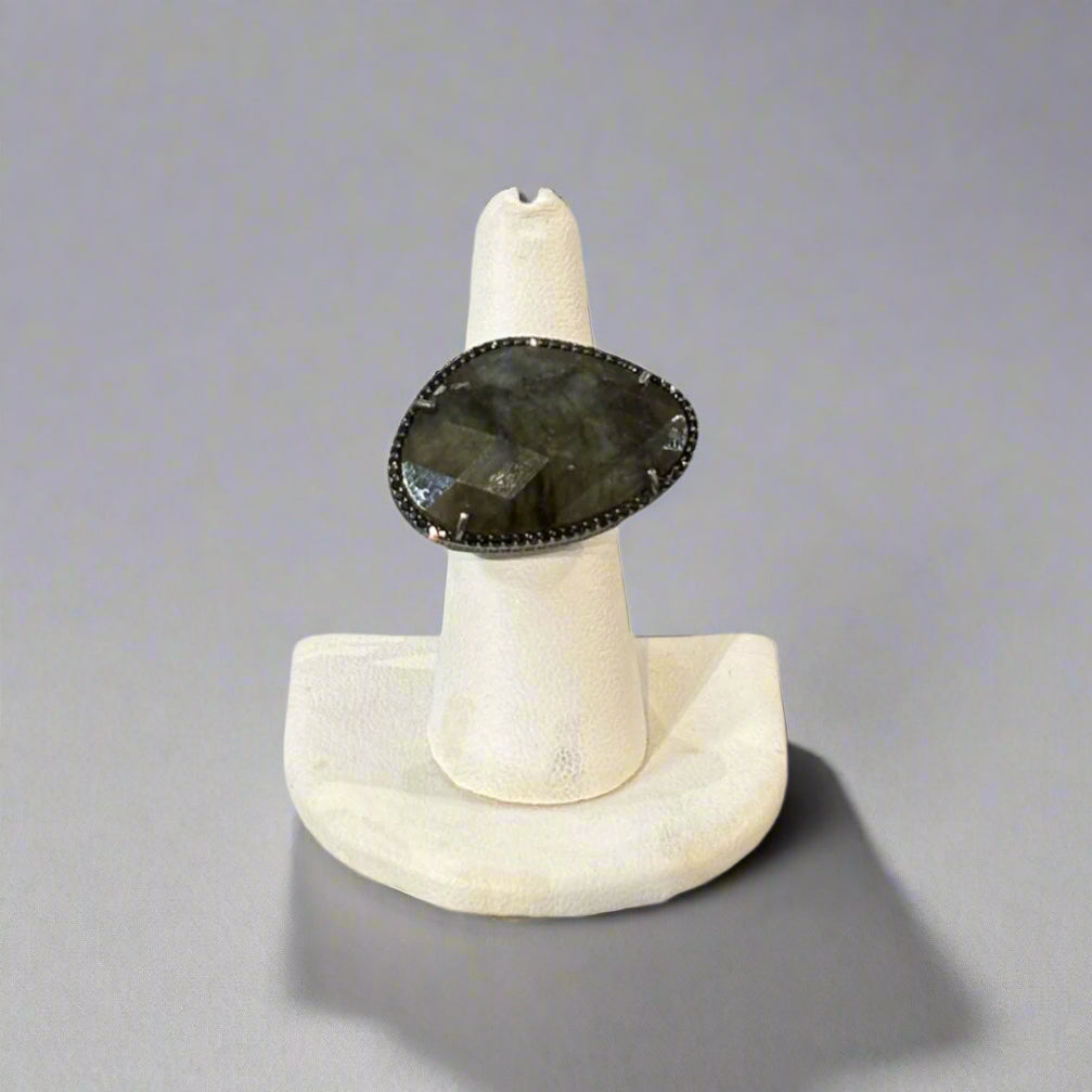 Ring with a dark stone on a white stand against a gray background