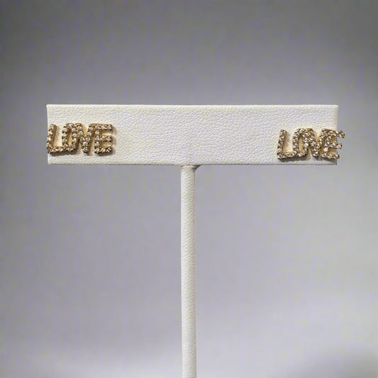 A silver-colored brooch with the word 'LOVE' in capital letters, featuring a textured surface and small gold-tone accents.