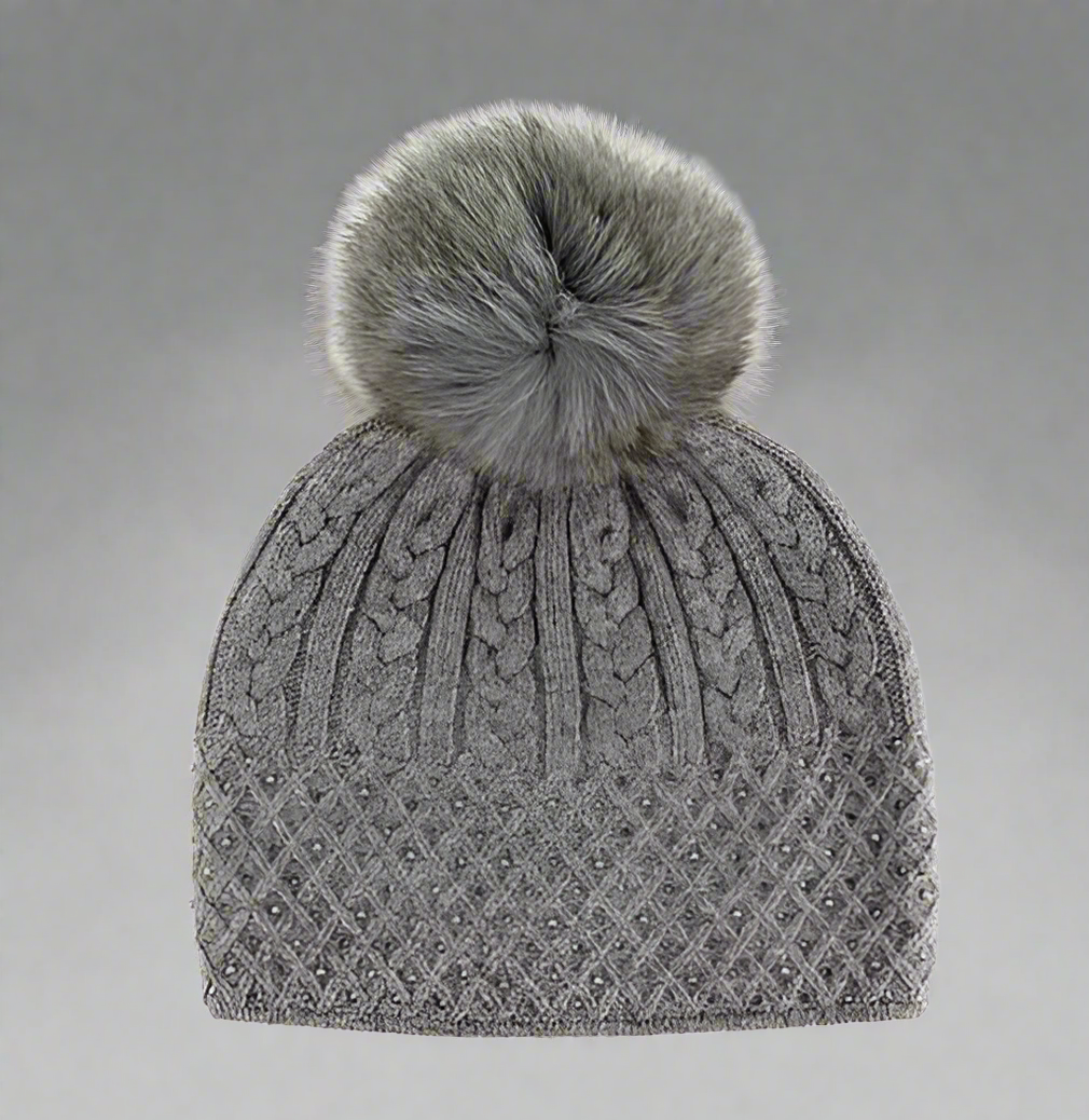 A gray cable knit sparkle hat with a fox fur pompom.