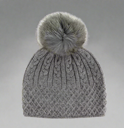 A gray cable knit sparkle hat with a fox fur pompom.