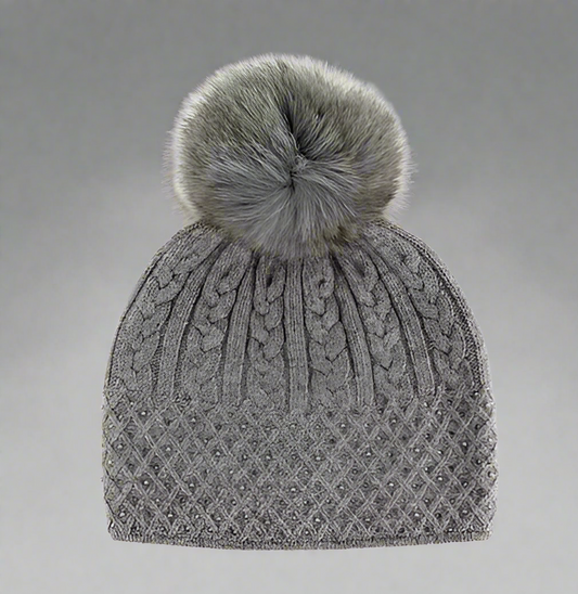 A gray cable knit sparkle hat with a fox fur pompom.