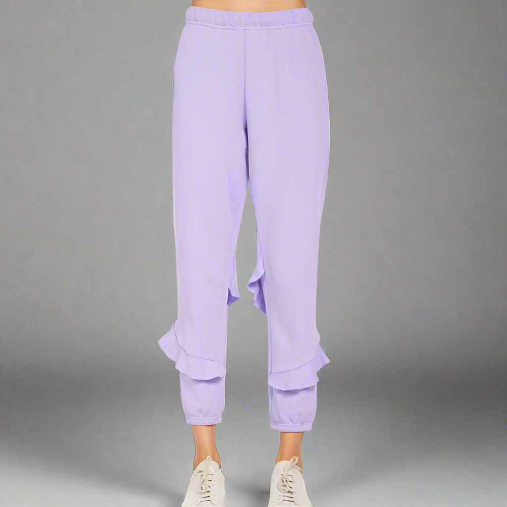 A person standing wearing purple ruffle sweatpants and white sneakers.